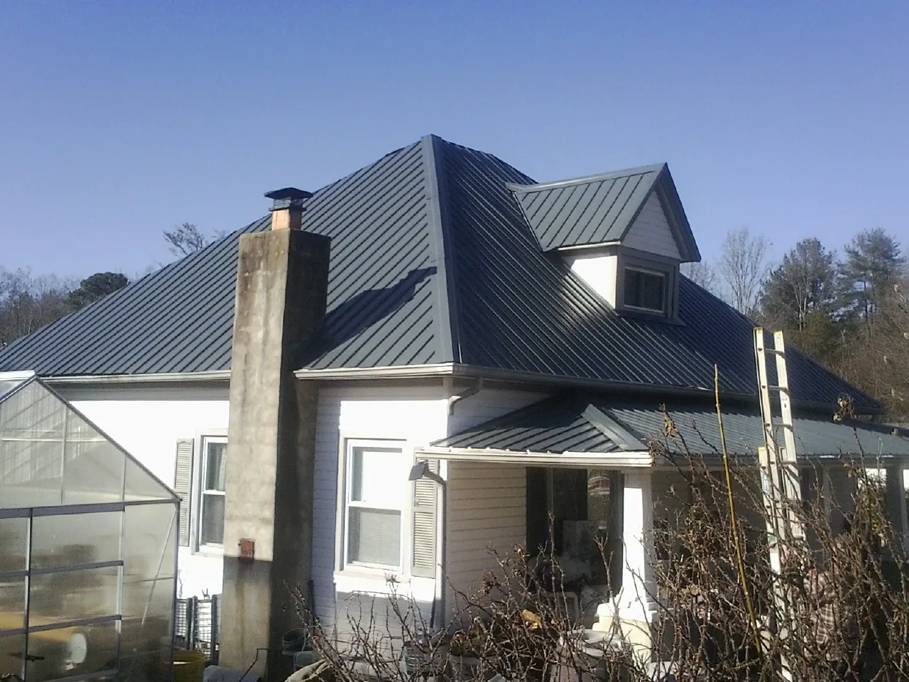Dark blue standing seam metal roof on a white farmhouse with dormer — Slate & Tile Roof Repair by Roofing Brothers in Mauston