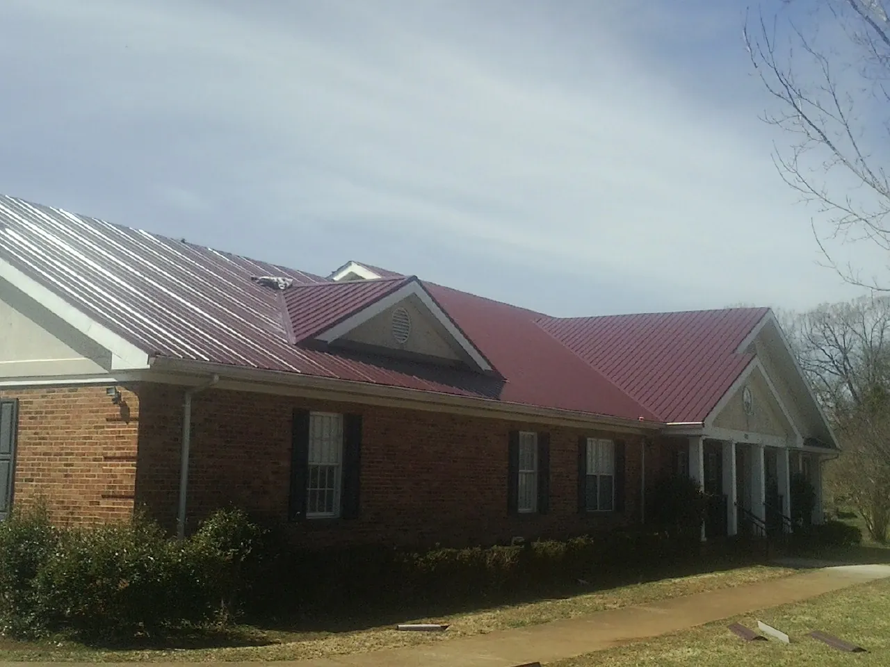 Red metal roof with gabled entries on a long brick building, from a Hail Damage Roof Repair job in Mauston