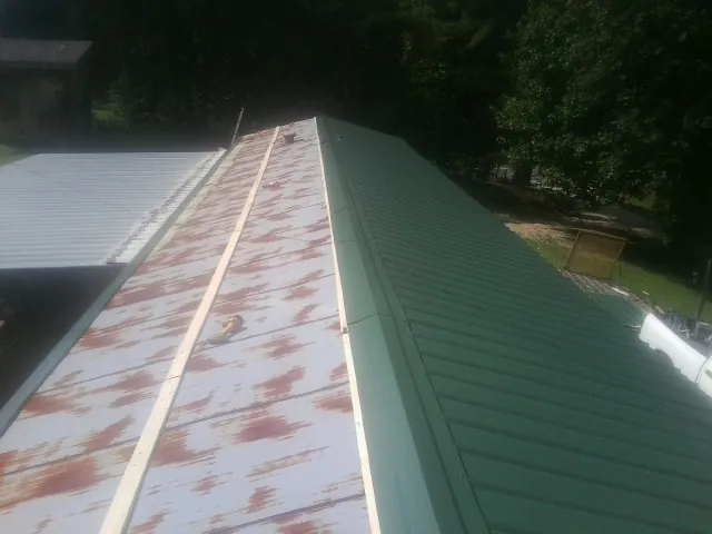 Old rusted panels beside newly installed green metal roofing — Wind Damage Roof Repair by Roofing Brothers in Mauston