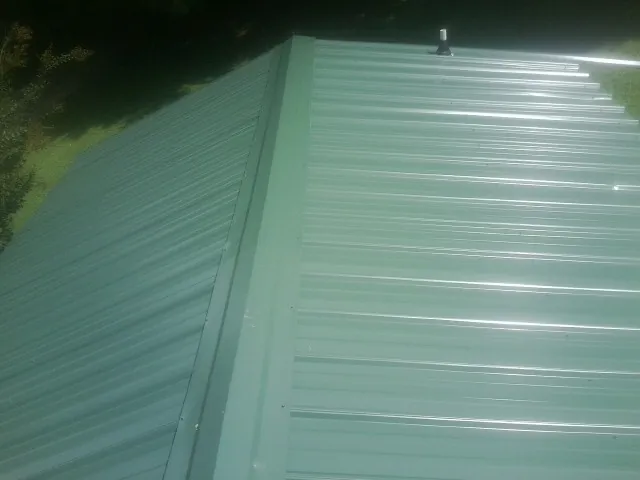 New green metal panels meeting at the ridge of a roof — Flat Roof Repair work by our crew in Mauston