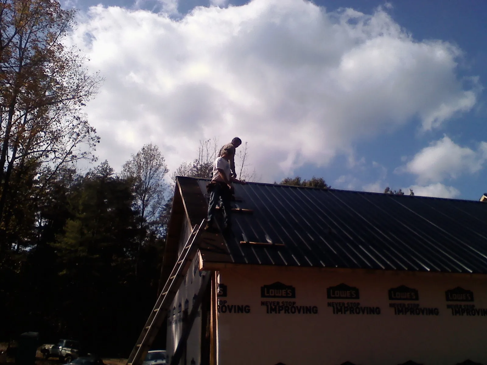 Roofer fastening dark metal panels high against a cloudy sky, from a Roof Inspection job in Mauston